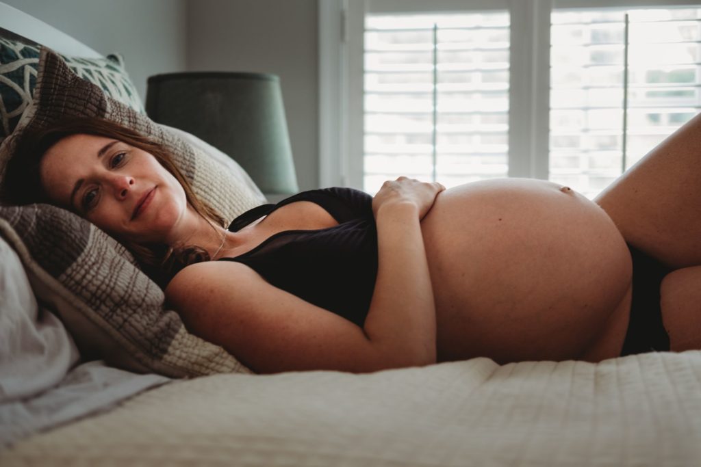 Best Maternity and Newborn Photographer Washington DC Virginia Maryland casual lifestyle in home maternity photography session pregnant woman lying on bed in black underwear in front of bright windows