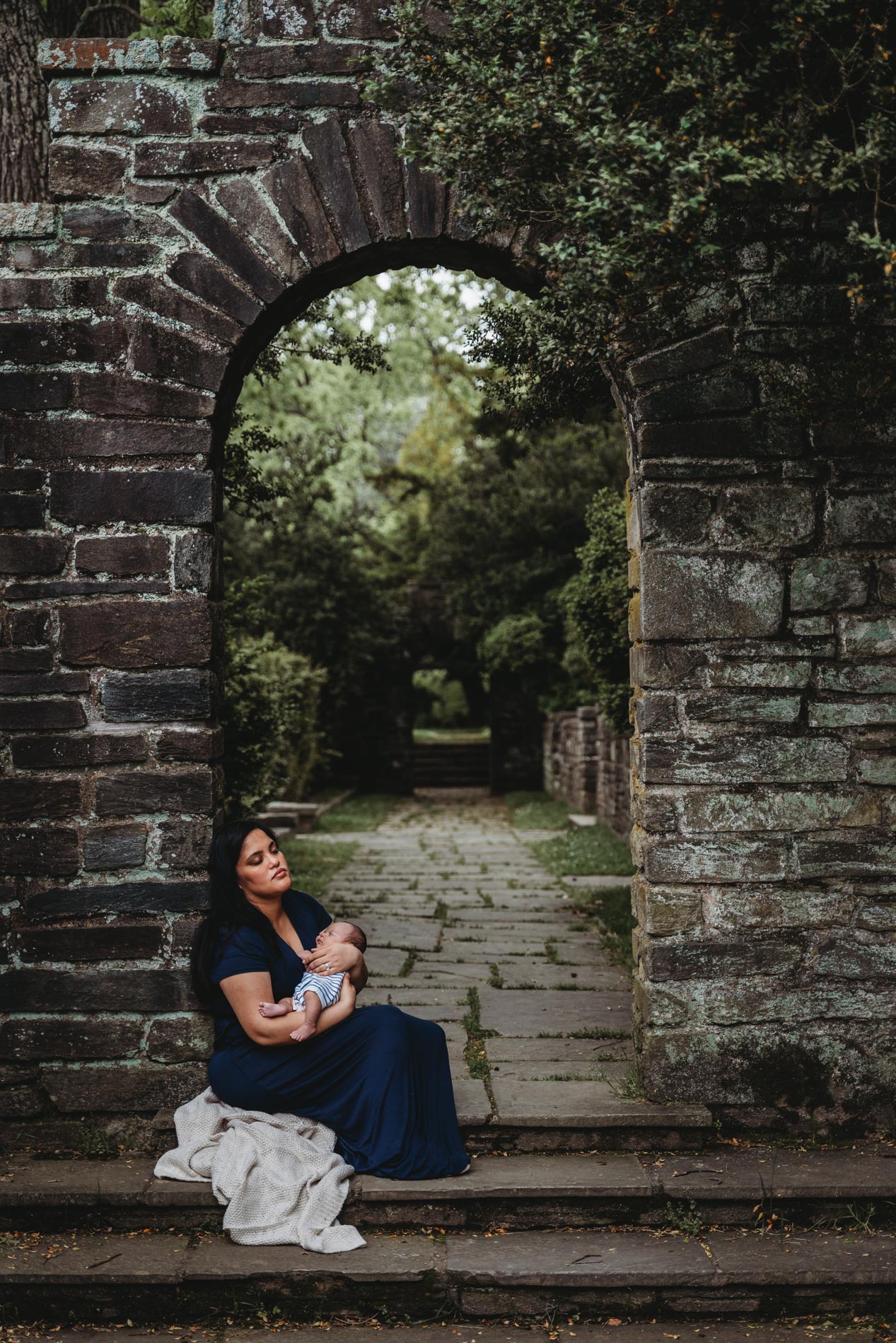 rockville maryland outdoor newborn photographer photography session montgomery county new mom in navy blue dress resting under stone archway with newborn