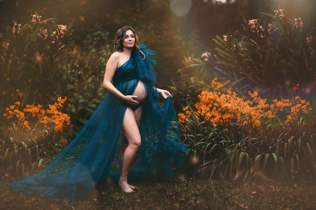 pregnant woman wearing teal tulle gown with belly showing in front of orange tiger lillies photographed by maternity photographer allison corinne