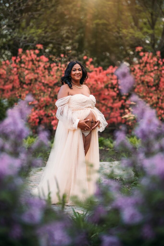 expecting mother in ivory dress surrounded by flowers photographed by maternity photographer allison corinne