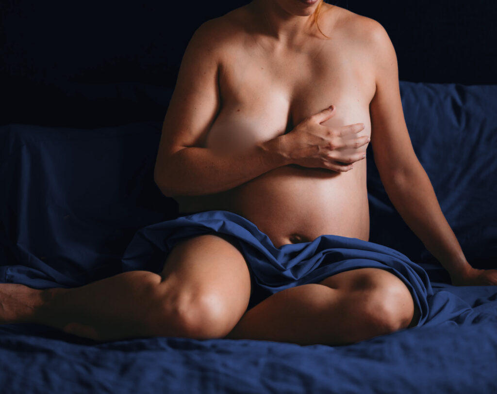nude pregnant woman on bed with dark blue sheets photographed by maternity photographer allison corinne